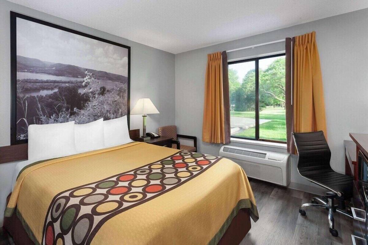 A hotel room with a bed, a desk, a chair, a window with curtains, and a wall-mounted picture.