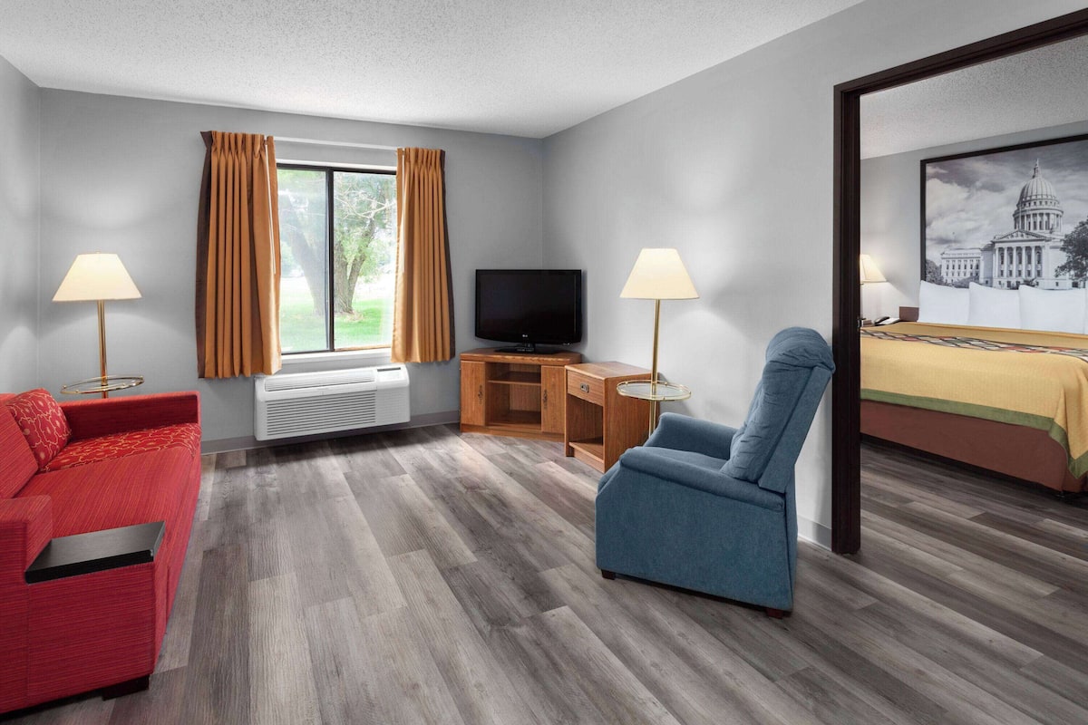 A hotel room with a red sofa, a blue armchair, a TV, a desk with a lamp, and a painting of a capitol building.