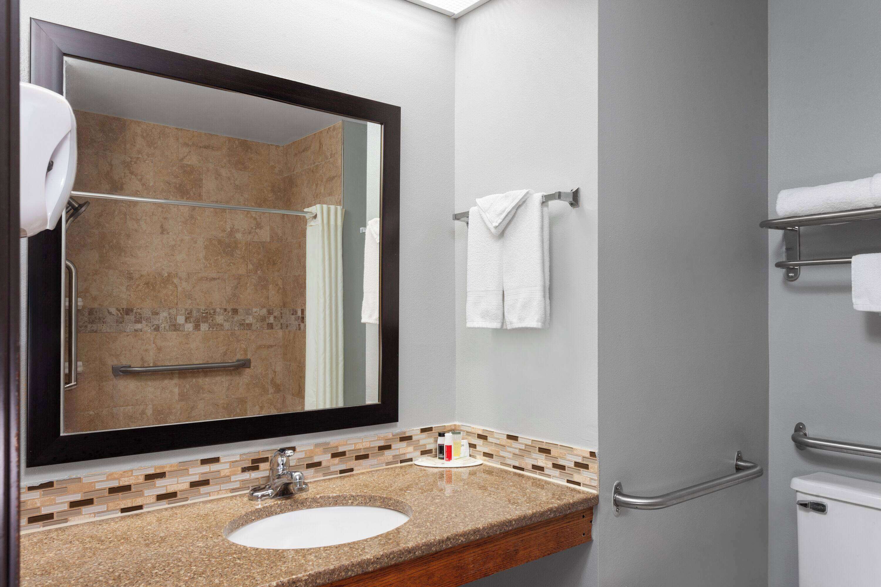 A bathroom with a large mirror, a sink, a towel rack, and a toilet.