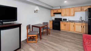 A compact living space with a TV, dining table, chairs, a kitchen area with wooden cabinets, a microwave, and a refrigerator. - Super 8 by Wyndham Sun Prairie/Madison E (Sun Prairie)