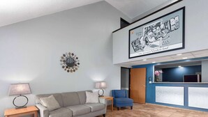 A reception area with a grey sofa, two side tables with lamps, a blue chair, and a reception desk with a blue wall. - Super 8 by Wyndham Sun Prairie/Madison E (Sun Prairie)
