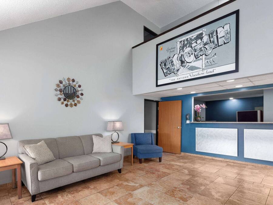 Un espace d’accueil avec un canapé gris, deux tables d’appoint avec des lampes, un fauteuil bleu et un comptoir d’accueil avec un mur bleu.
