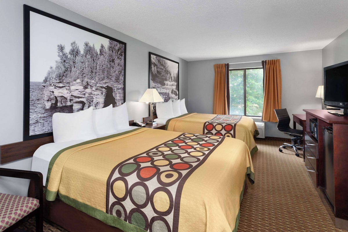 A hotel room with two beds, a desk, a television, and a window with curtains.