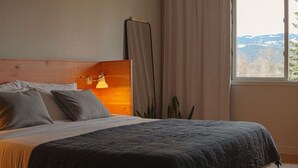 A bedroom with a bed, a bedside lamp, a window with curtains, and a view of the outdoors.