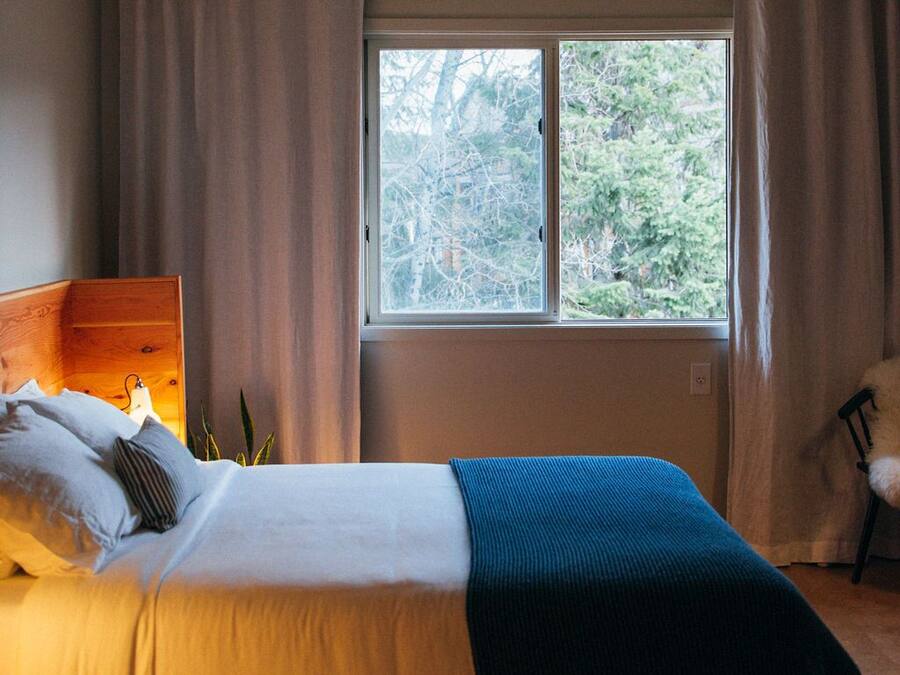 A bedroom with a wooden bed, a nightstand, a window with curtains, and a view of trees outside.