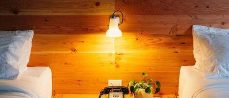 A room with two beds, a wooden headboard, a bedside table with a lamp, a telephone, and a framed picture on the wall.