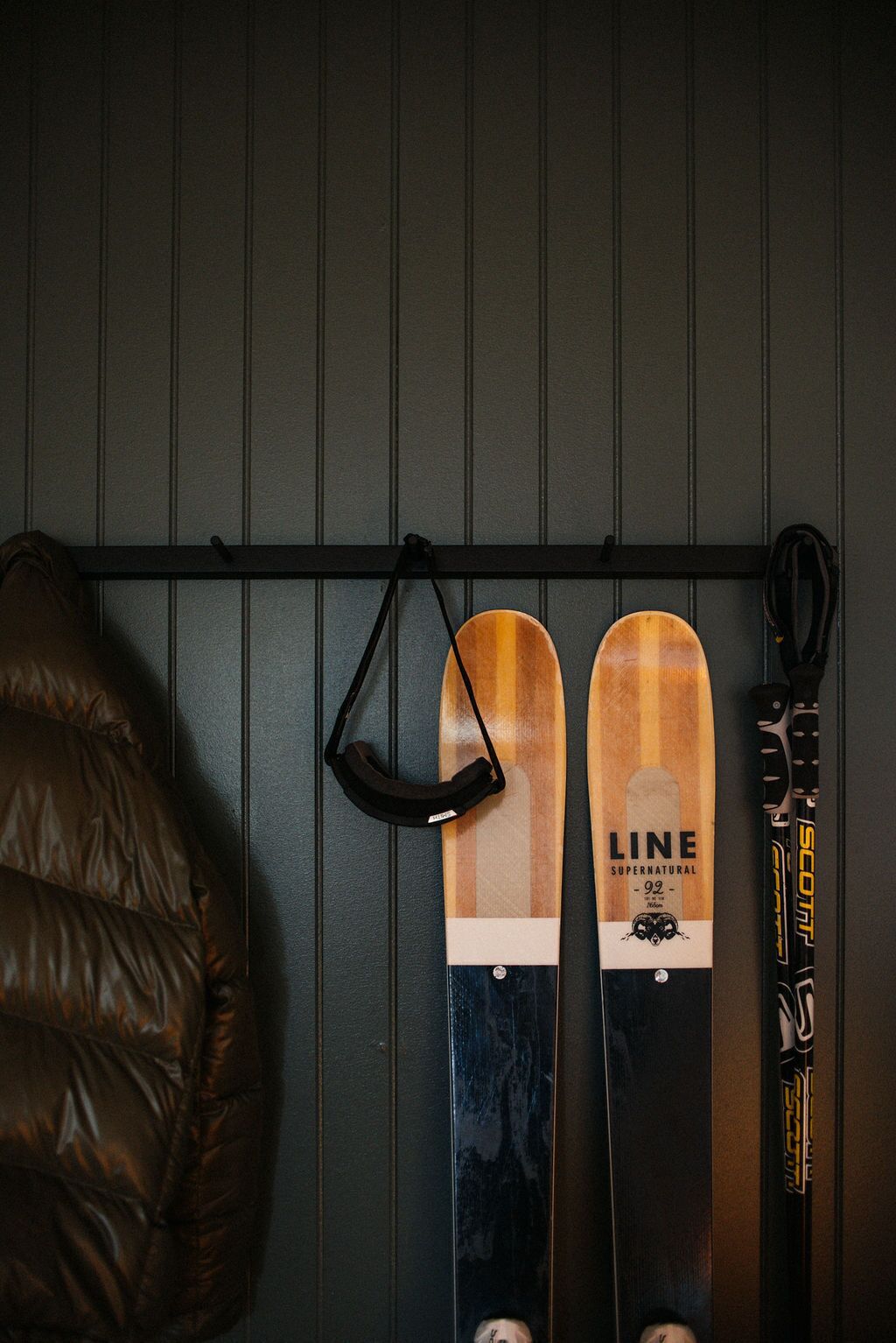 Zwei Ski an einer Wand, ein Paar schwarze Skischuhe und eine braune Jacke.