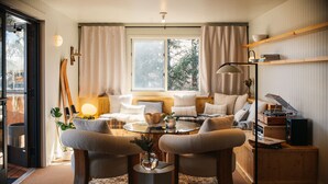 A cozy living room with a round coffee table, two armchairs, a sofa, and a bookshelf.