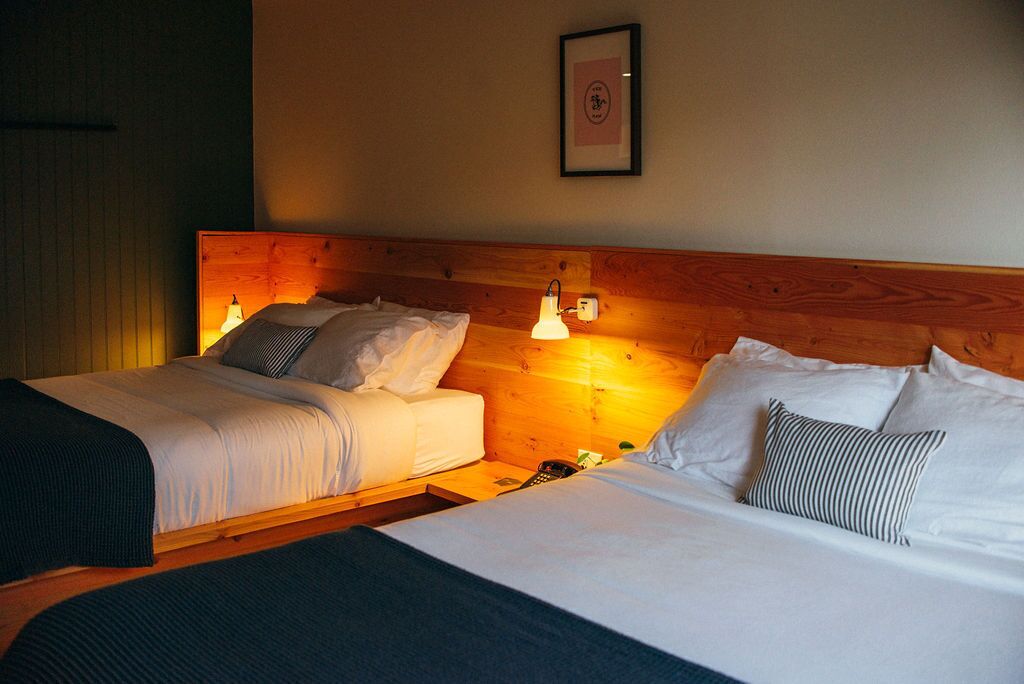 A hotel room with two beds, wooden headboard, bedside lamps, and a framed picture on the wall.