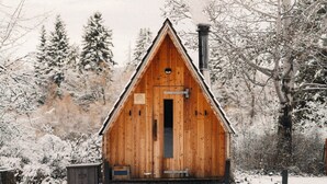 A wooden cabin with a triangular roof, a chimney, and a door with a small window above it.