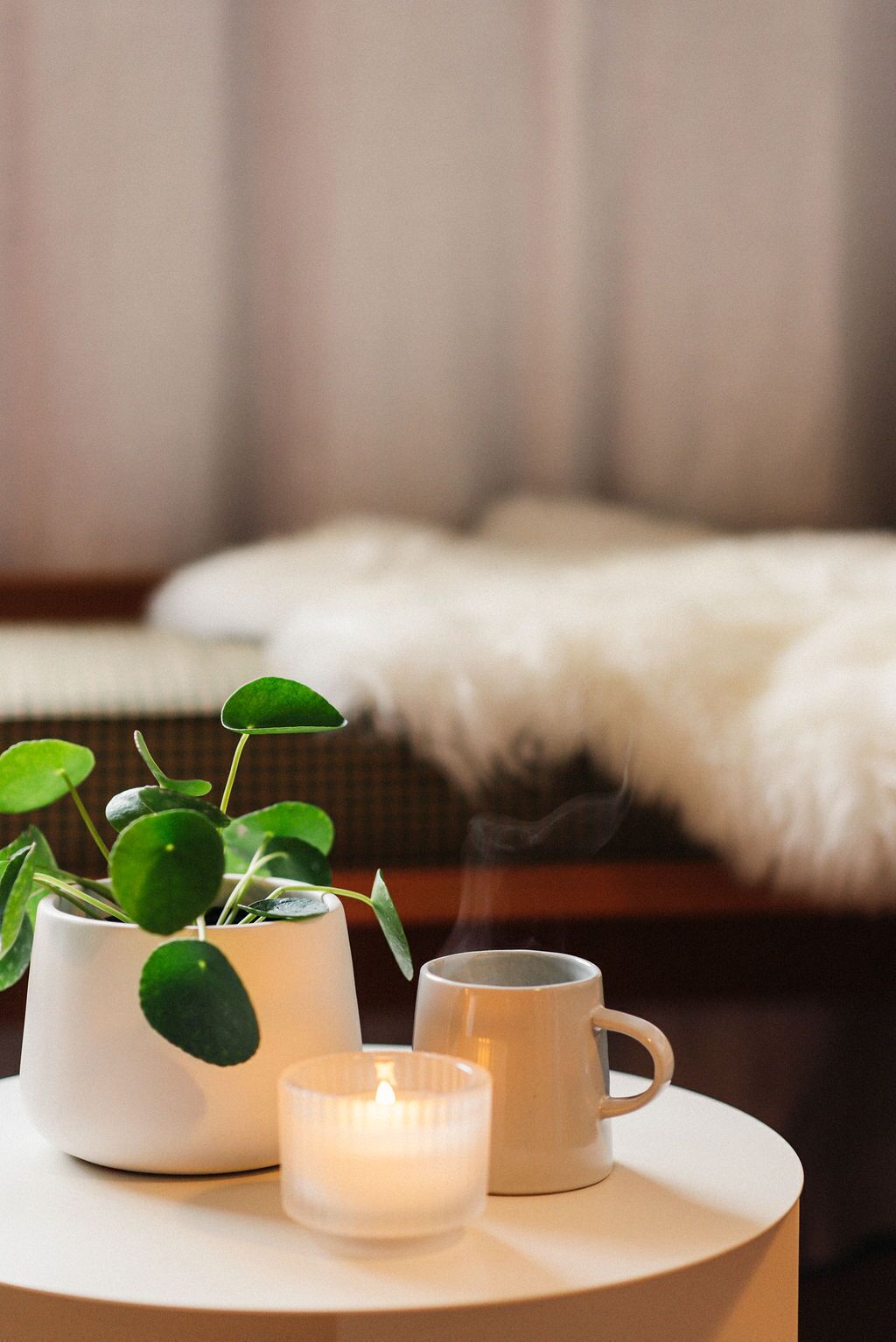 Un intérieur chaleureux avec une tasse blanche, une petite bougie et une plante en pot placés sur une table ronde.