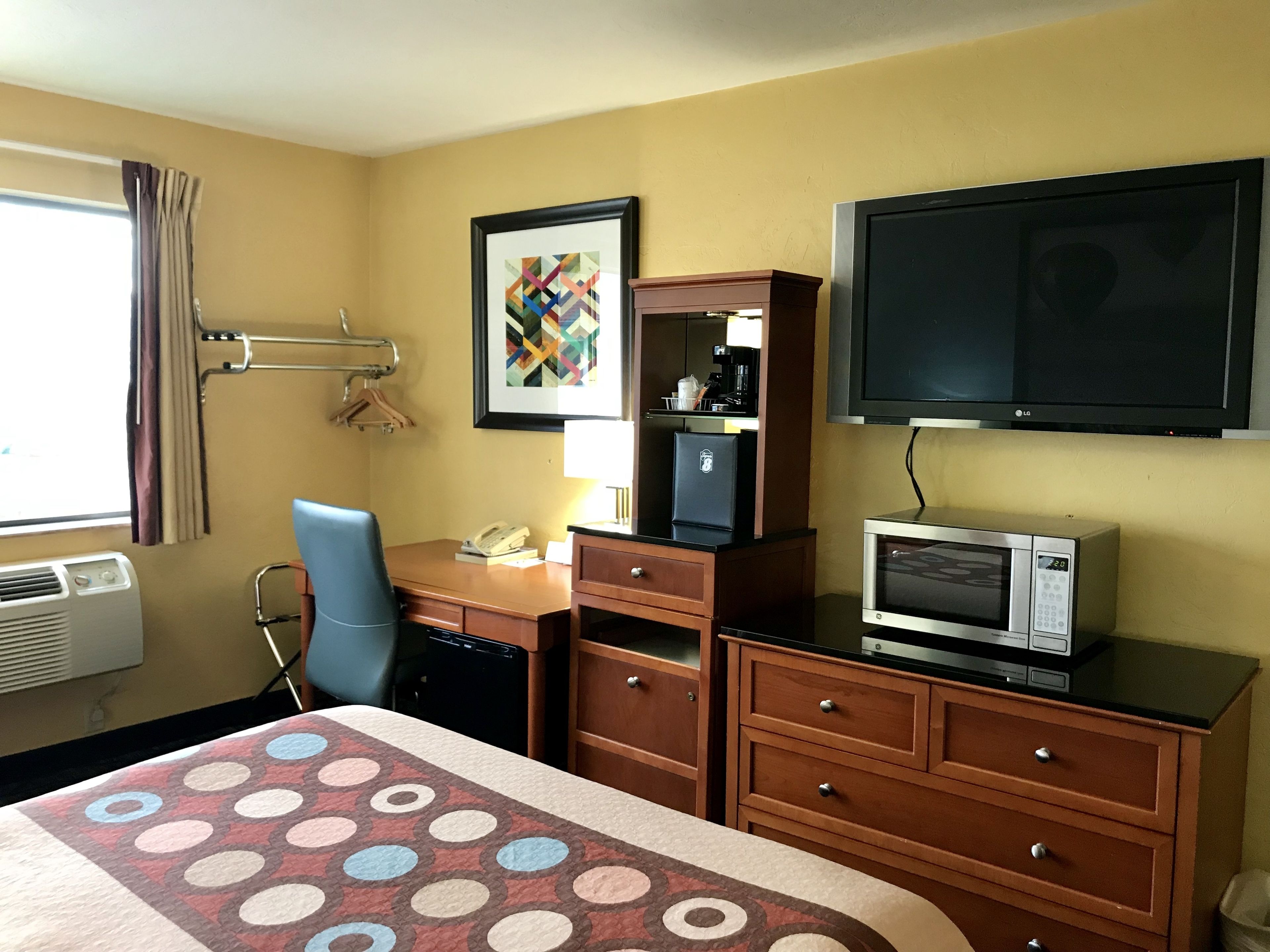 A hotel room with a bed, a desk with a telephone, a microwave, a TV, and a window with curtains.