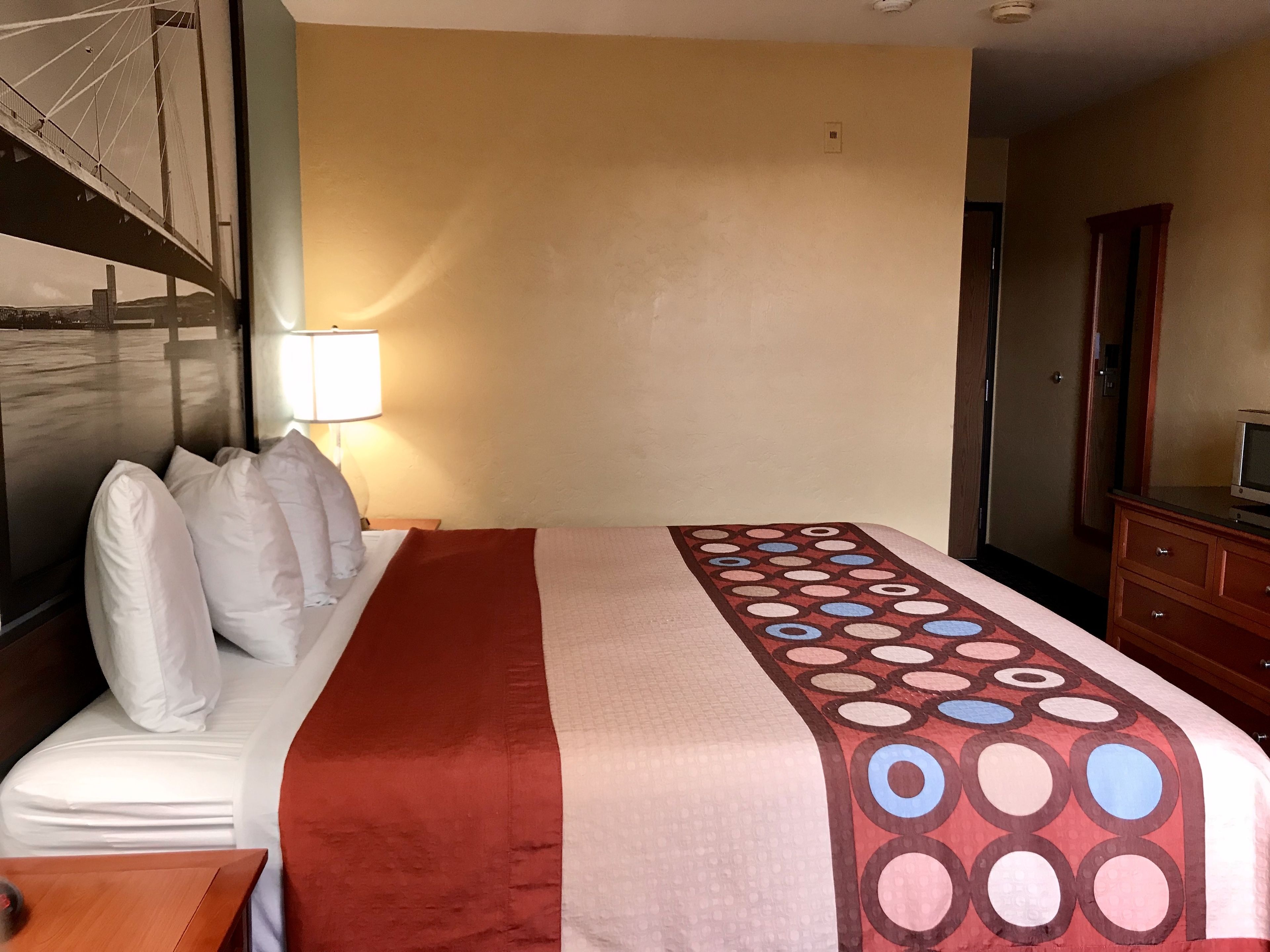 Una habitación de hotel con una cama, una mesita de noche con lámpara, un aparador y un espejo.
