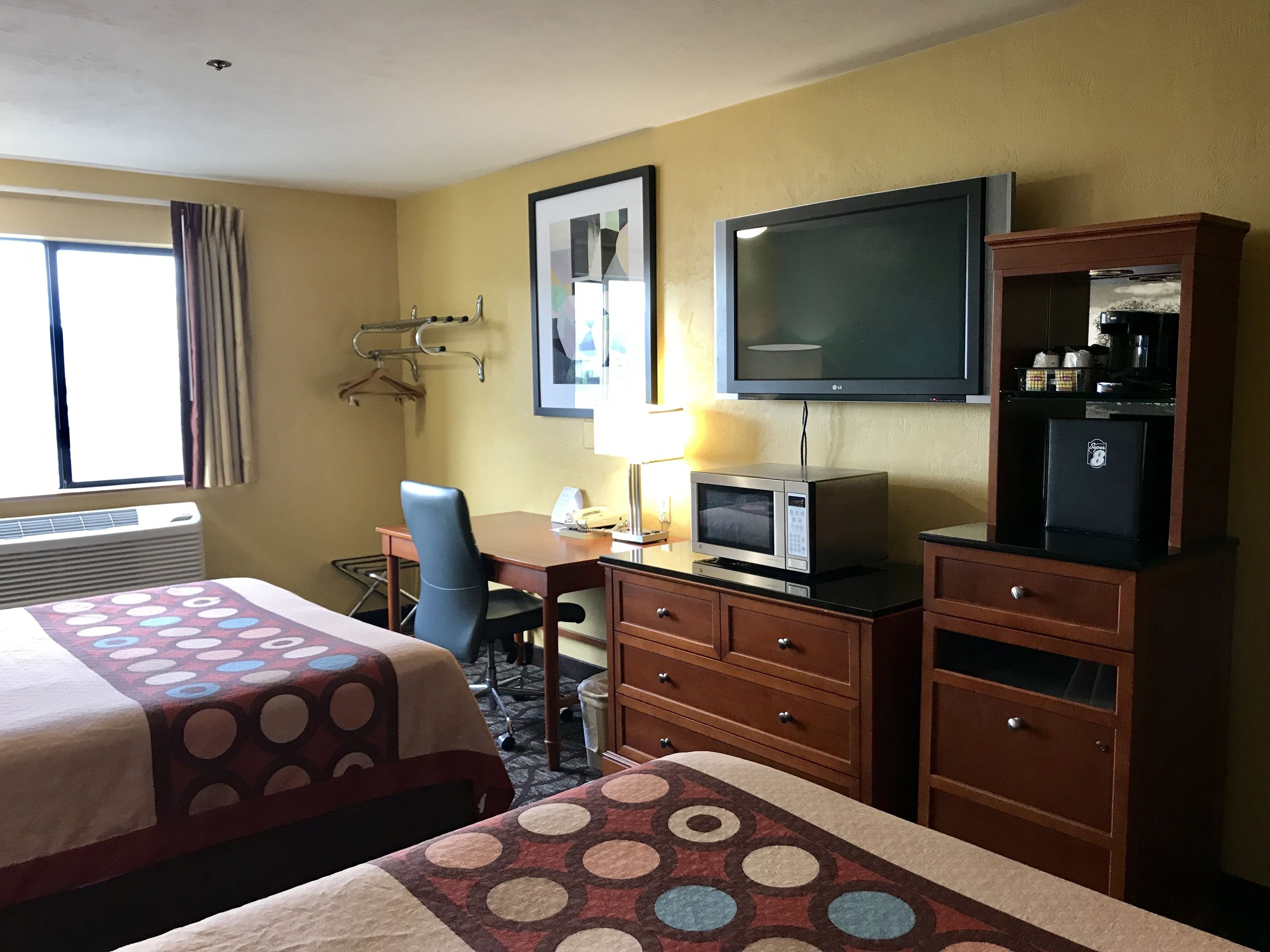 Habitación de hotel con dos camas, un escritorio, televisión, microondas, refrigerador y ventana con cortinas.