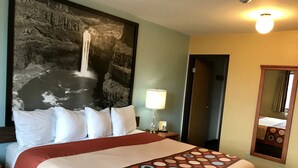 Ein Hotelzimmer mit einem großen Bett, einem Kopfteil mit einem Wasserfallgemälde, einer Nachttischlampe und einem Spiegel an der Wand.