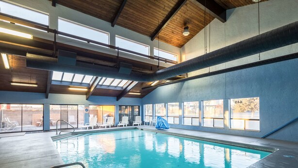 En indendørs swimmingpool med krystalklart vand, træbjælker i loftet og store vinduer der lukker naturligt lys ind.