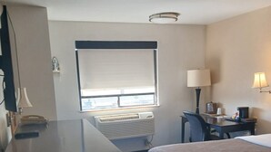 Et hotelværelse med seng, skrivebord, lampe, klimaanlæg og et vindue med persienner.