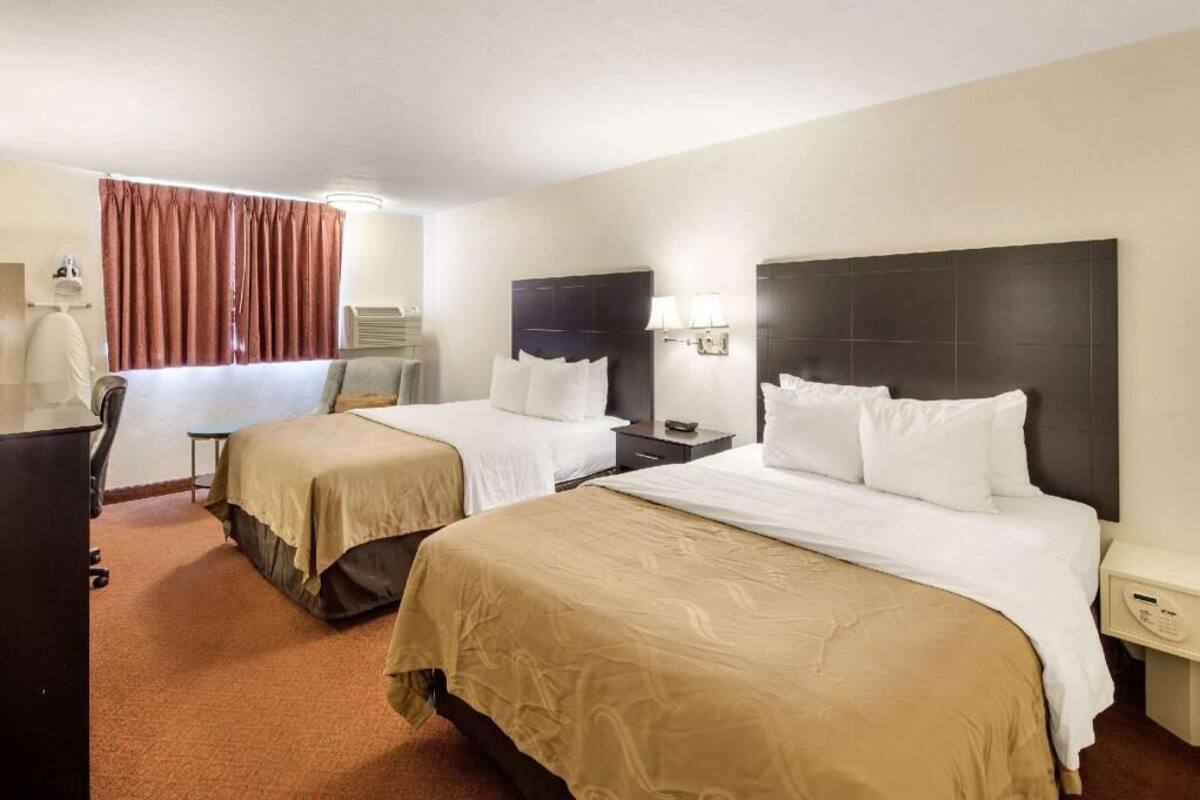 Una habitación de hotel con dos camas, un escritorio, una silla, una lámpara y una ventana con cortinas.
