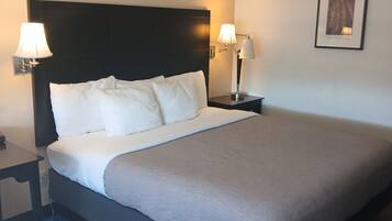 Un cuarto de hotel con una cama grande, dos lámparas de noche, una mesita y un cuadro en la pared.