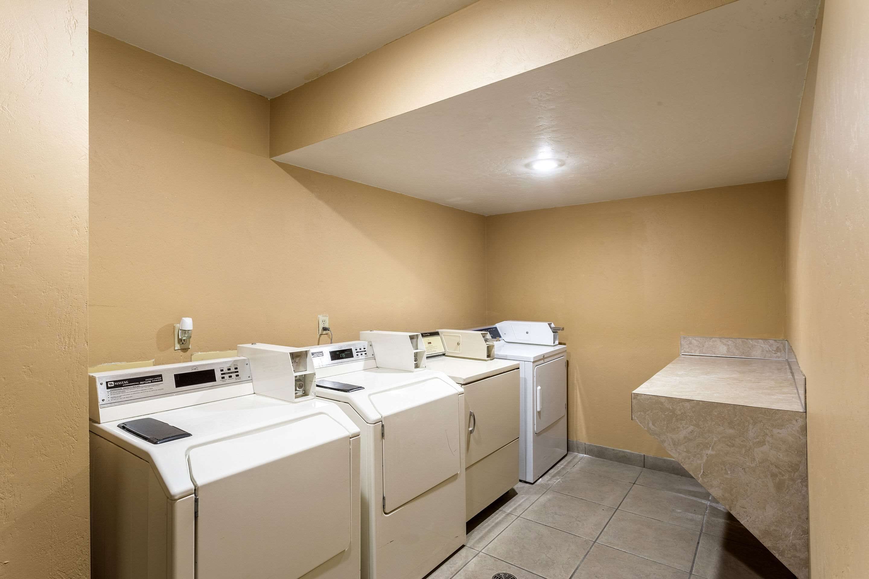 A laundry room with four white washers and dryers, a small sink, and a tiled floor.