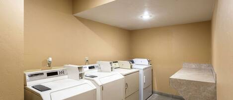 A laundry room with four white washers and dryers, a small sink, and a tiled floor.