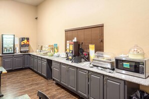 A kitchen area with a microwave, toaster, and coffee maker. There are also various food items and condiments on the counter.