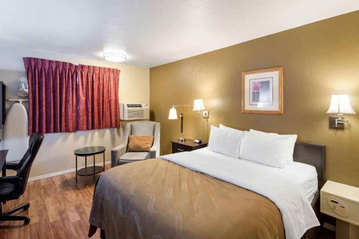 Una habitación de hotel con cama, una silla, una mesa, una lámpara y un cuadro en la pared.