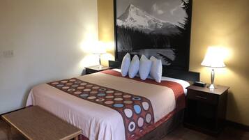 A hotel room with a bed, two bedside tables, a nightstand, a bench, and a large painting on the wall.
