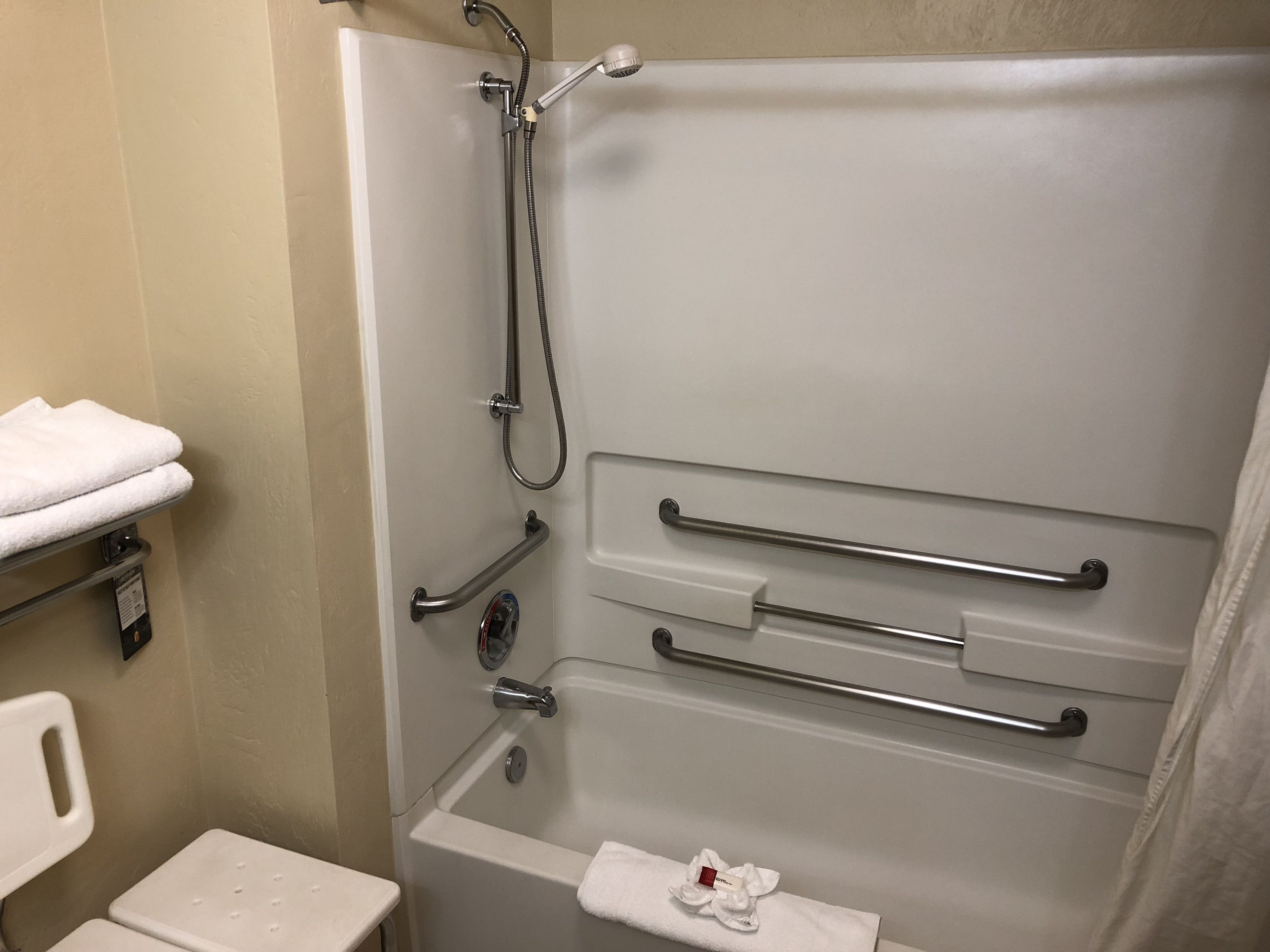 Un baño con bañera, barras de apoyo, toallero y retrete.