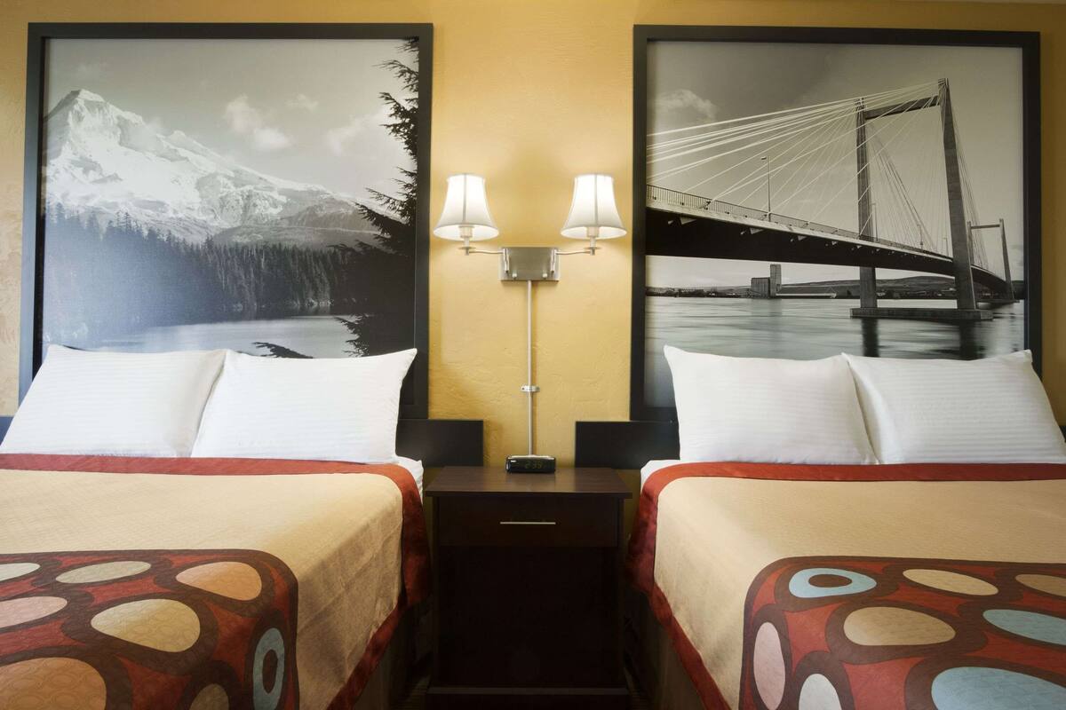 A hotel room with two beds, each with a patterned bedspread, a nightstand with a lamp, and two framed pictures on the wall.