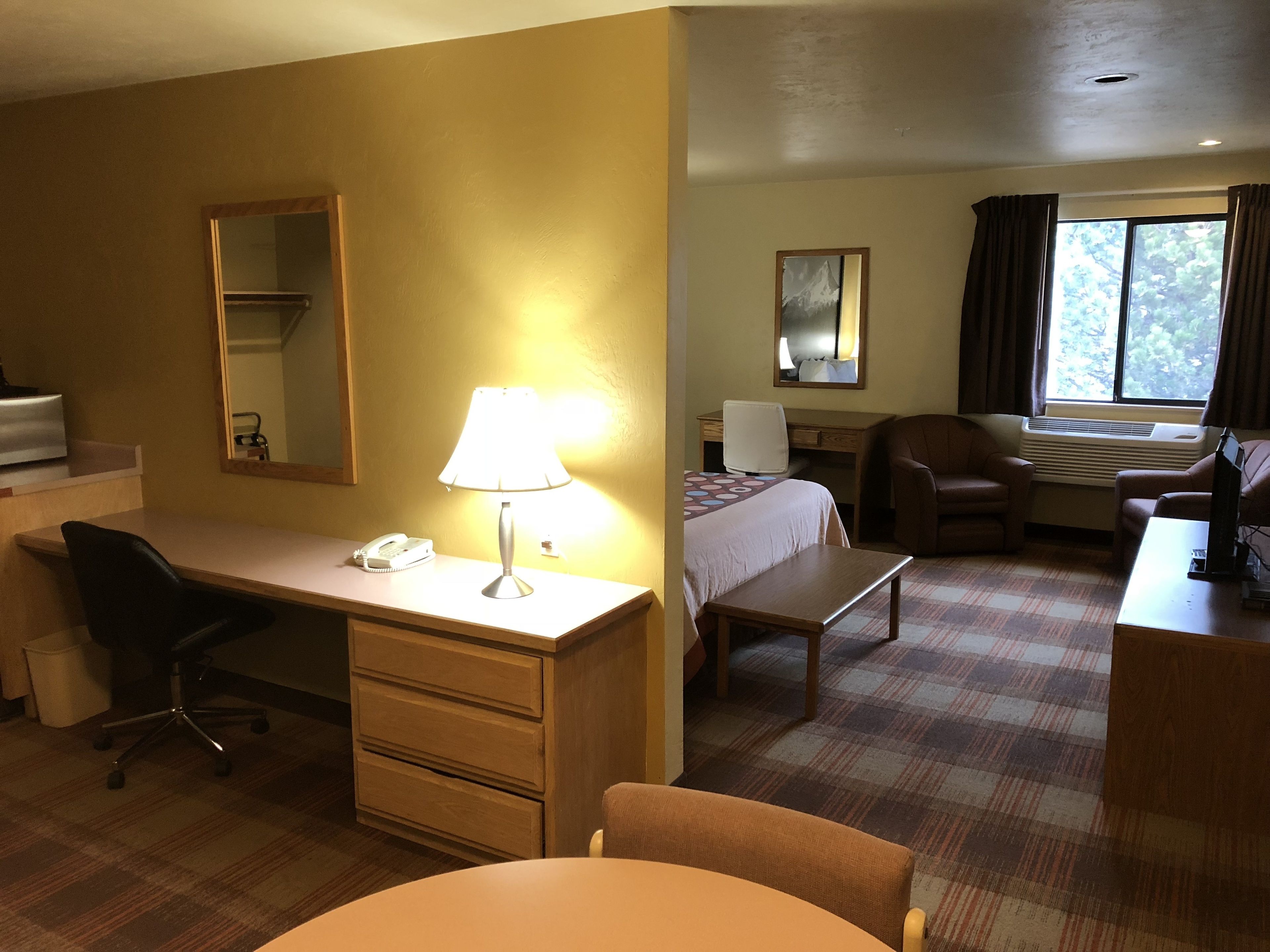Habitación de hotel con escritorio, silla, cama y ventana con cortinas.
