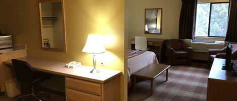 A hotel room with a desk, chair, bed, and a window with curtains.