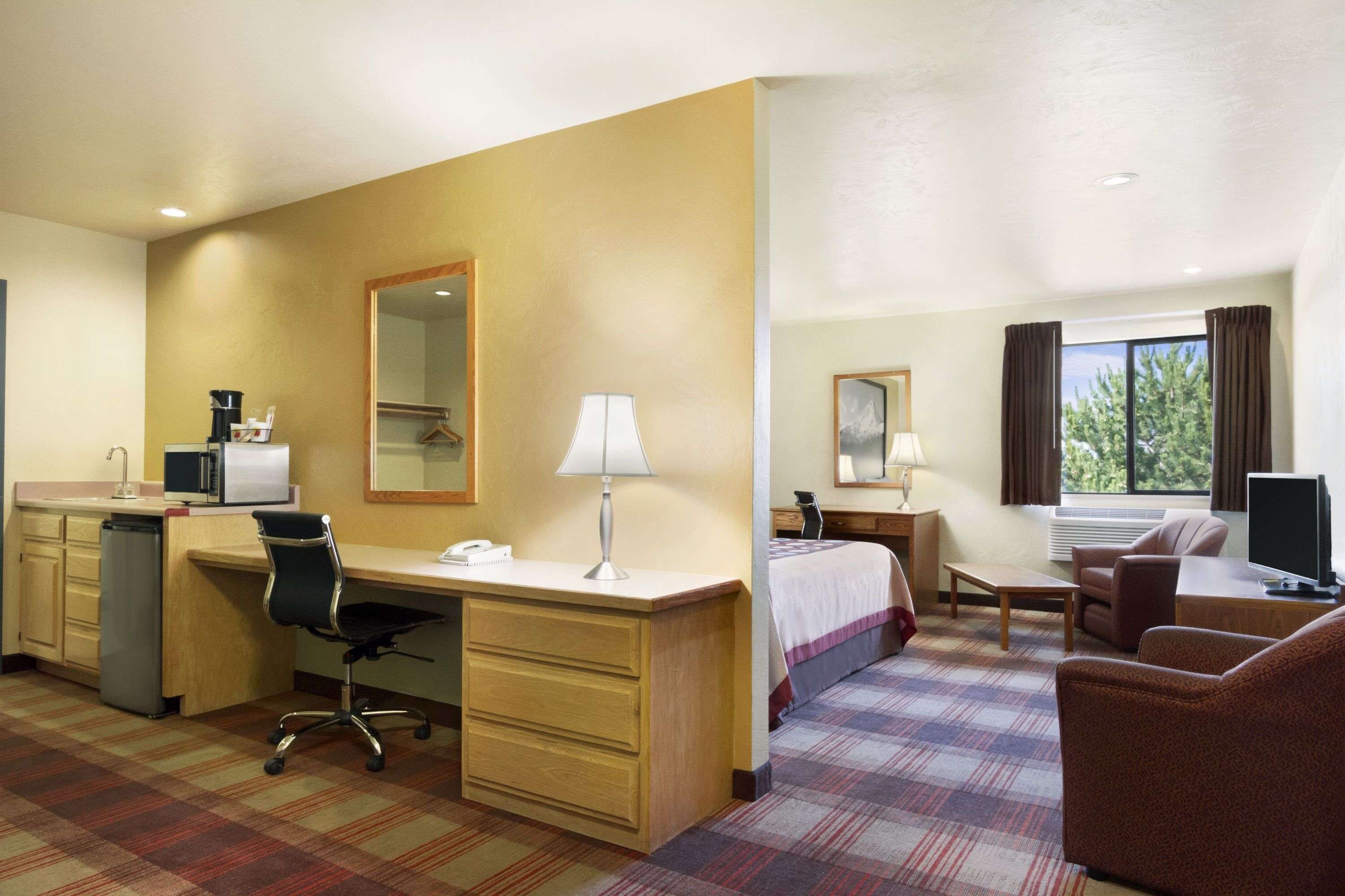 A hotel room with a desk, chair, bed, and a TV.