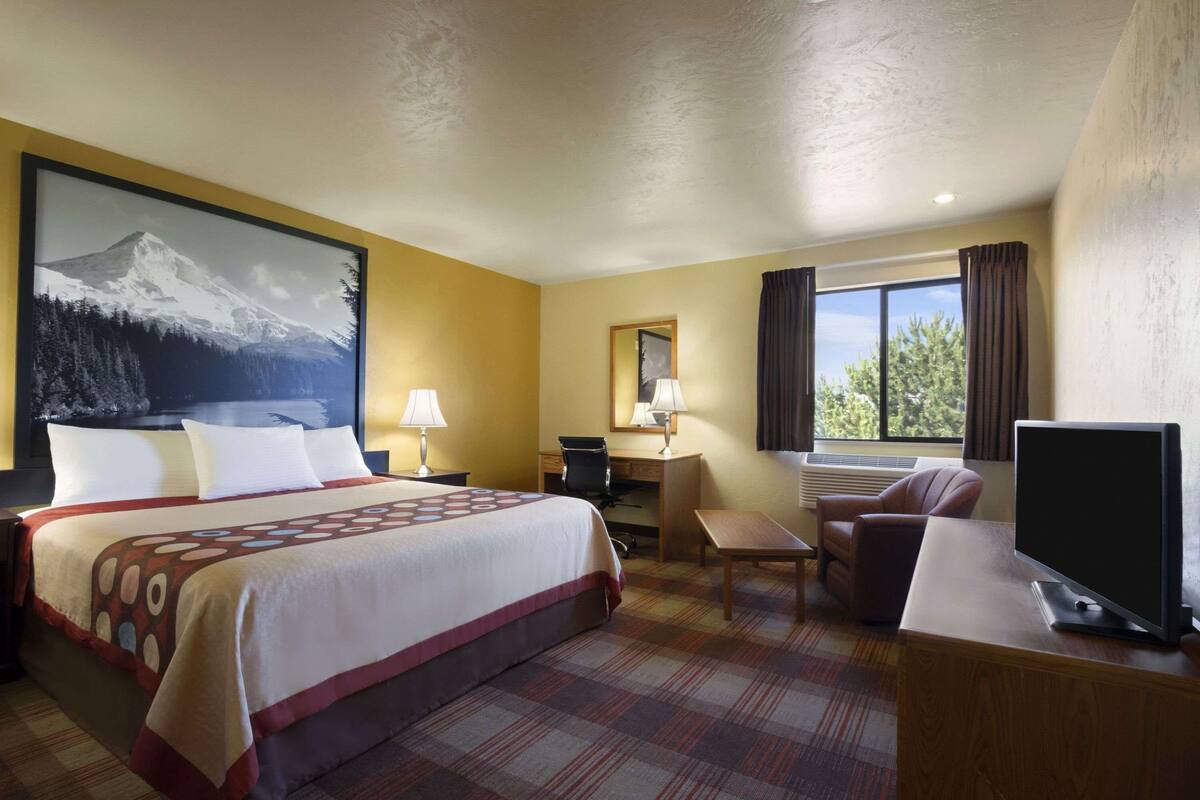 A hotel room with a bed, desk, chair, TV, and a large window with curtains.