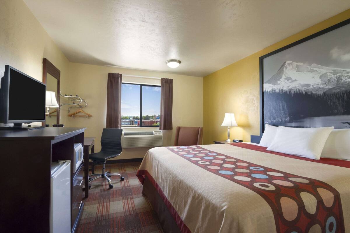 A hotel room with a bed, desk, chair, and a large window.