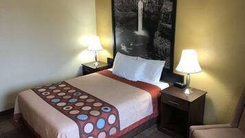 A hotel room with a bed, two bedside tables with lamps, a chair, a large abstract painting on the wall, and a patterned bedspread.