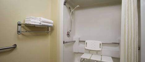 A bathroom with a shower, grab bars, a white chair, and a towel rack.