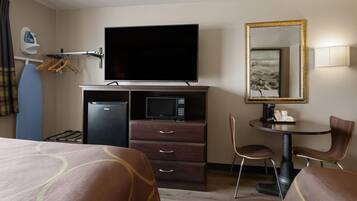 Habitación de hotel con cama, escritorio, televisor, microondas, refrigerador, silla y espejo.