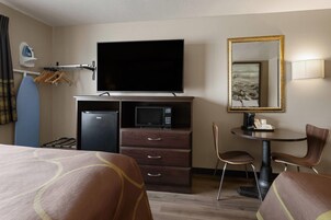 Habitación de hotel con cama, escritorio, televisor, microondas, refrigerador, silla y espejo.