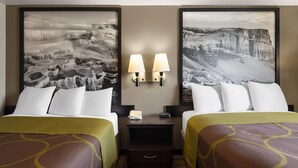Una camera d'albergo con due letti, un comodino con lampade e due grandi fotografie incorniciate alle pareti.