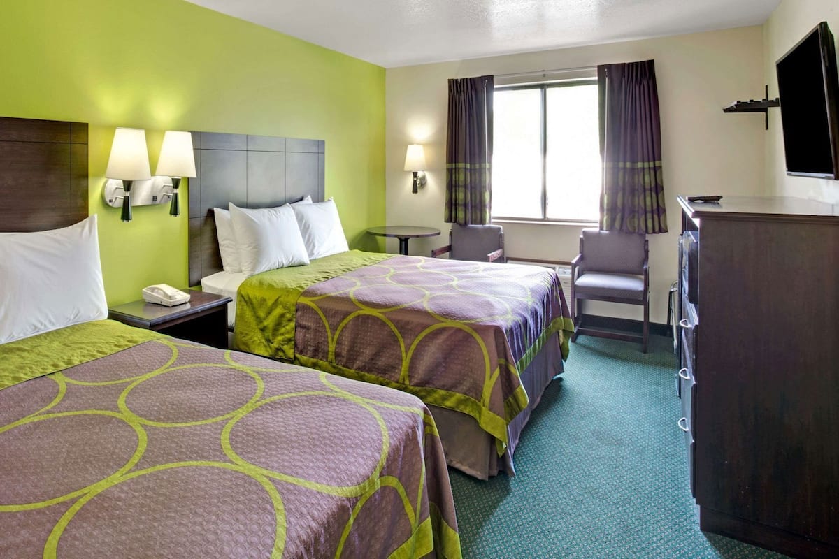 A hotel room with two beds, a desk, a chair, a TV, and a window with curtains.