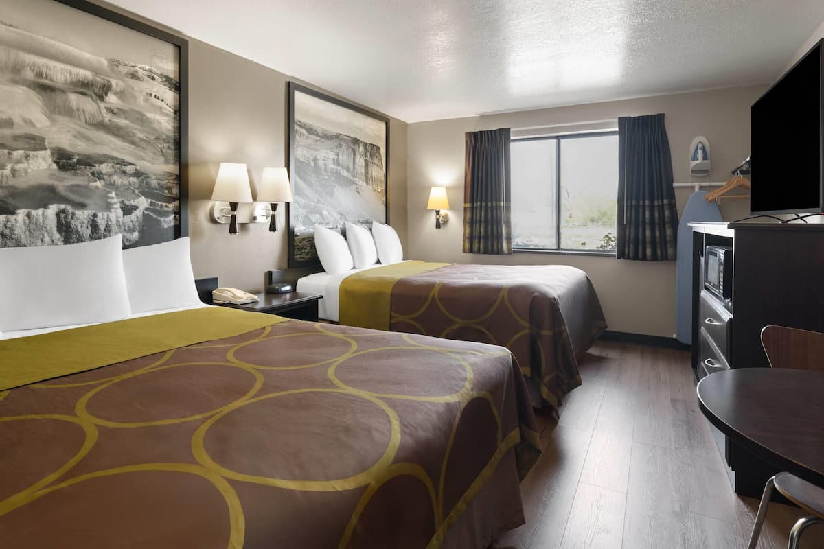 A hotel room with two beds, a desk, a chair, a TV, and a window with curtains.