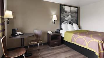 Una habitación de hotel con cama, un escritorio con lámpara, una silla, una mesita de noche con teléfono y una lámpara de pared.