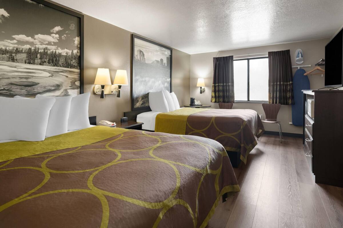 A hotel room with two beds, a desk, a chair, a TV, and a painting on the wall.