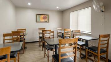 A room with wooden chairs and tables, a painting on the wall, and a window with blinds.
