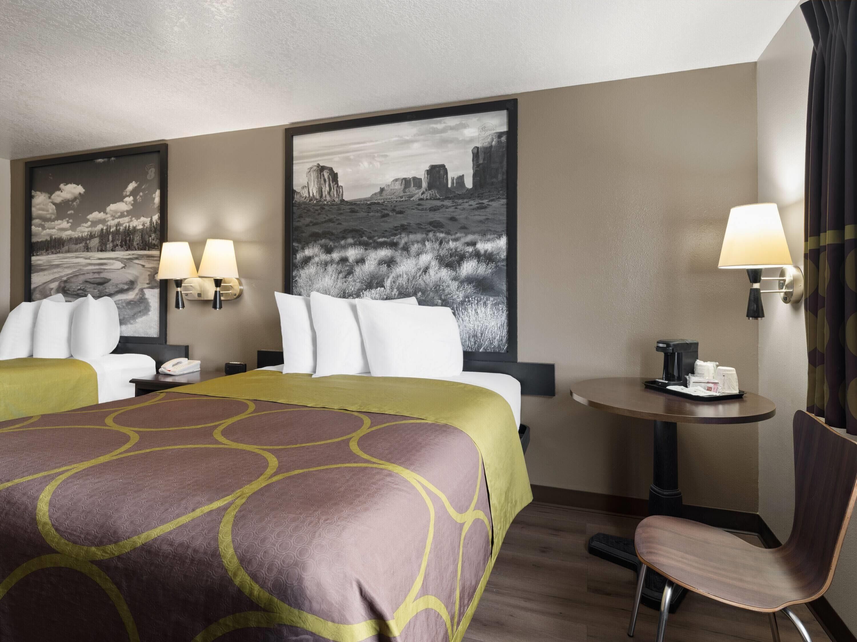 Una habitación de hotel con una cama grande, dos lámparas de noche, una mesita con lámpara, una silla y dos lámparas de pared.