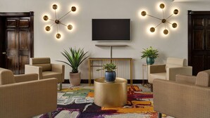 A living room with beige sofas, a TV mounted on the wall, and a colorful rug. - Super 8 by Wyndham Ocean Springs Biloxi (Ocean Springs)