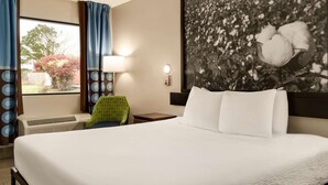 A hotel room with a large bed, a desk, a chair, a window with curtains, a wall-mounted lamp, and a framed picture of cotton plants. - Super 8 by Wyndham Ocean Springs Biloxi (Ocean Springs)