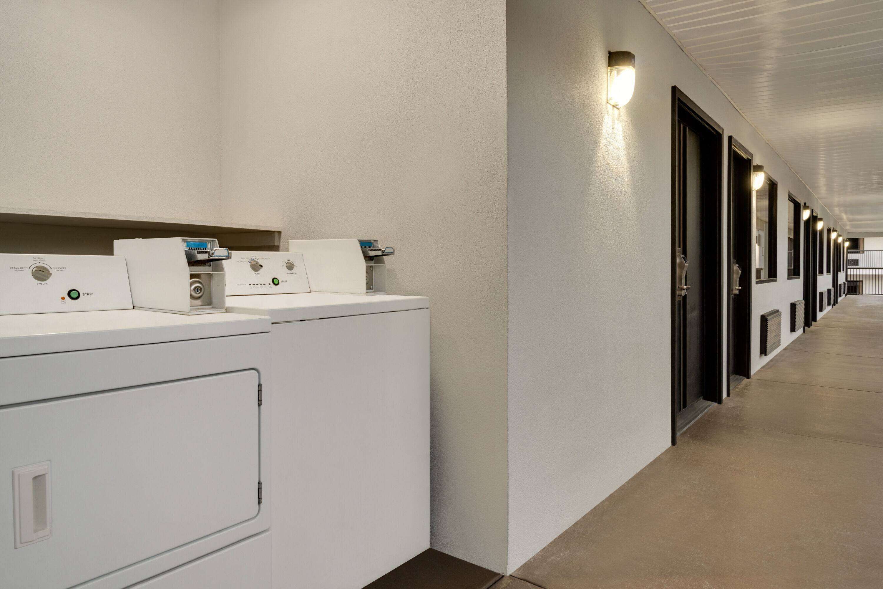 Un couloir d’hôtel bordé de rangées de machines à laver blanches et de portes.