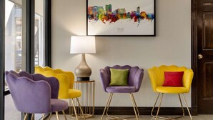 A room with a city skyline artwork, a lamp, and a set of four chairs with gold legs. - Super 8 by Wyndham Ocean Springs Biloxi (Ocean Springs)